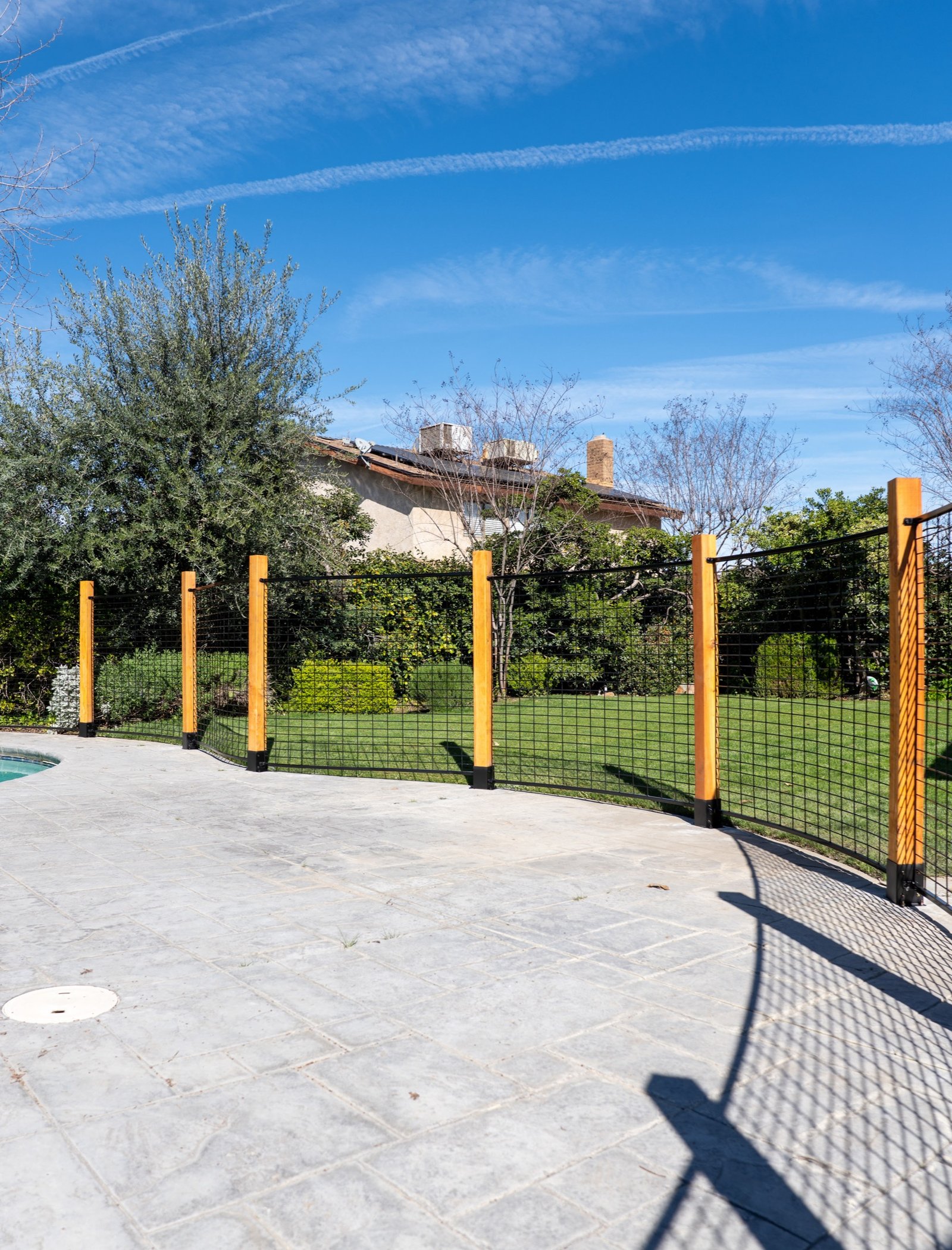 Curved black hog panel pool fence showing wood post spacing, patio edge transitions, and open-view welded wire panels